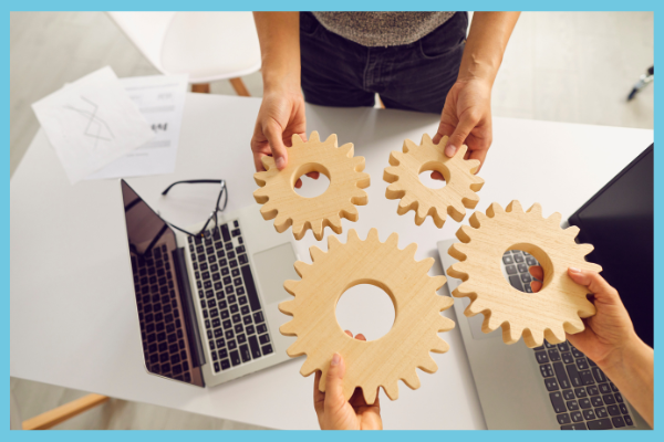 Colleagues holding wooden cogs over laptops